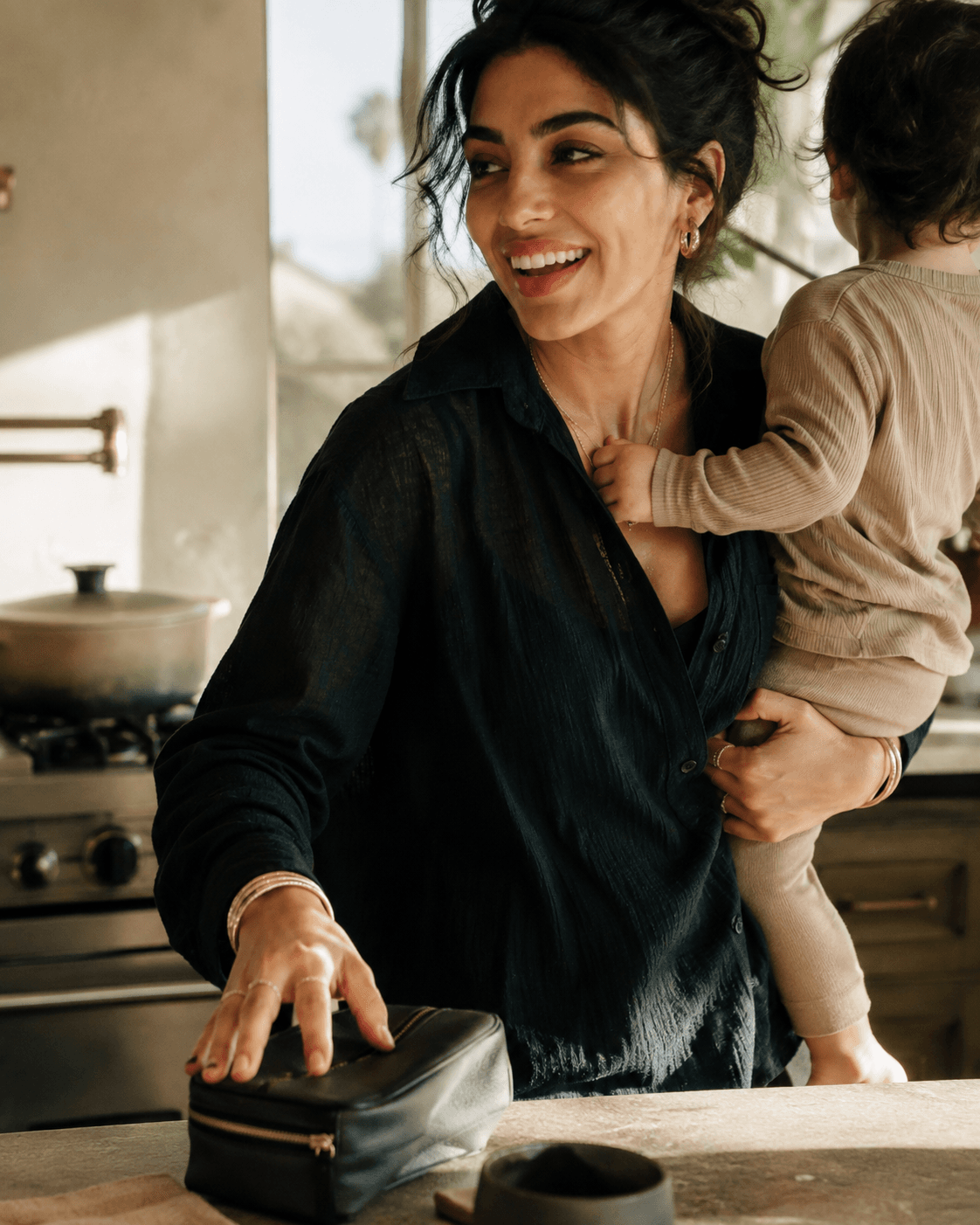 Temporary lifestyle frame: a woman holding a baby on her hip in a sunlit kitchen