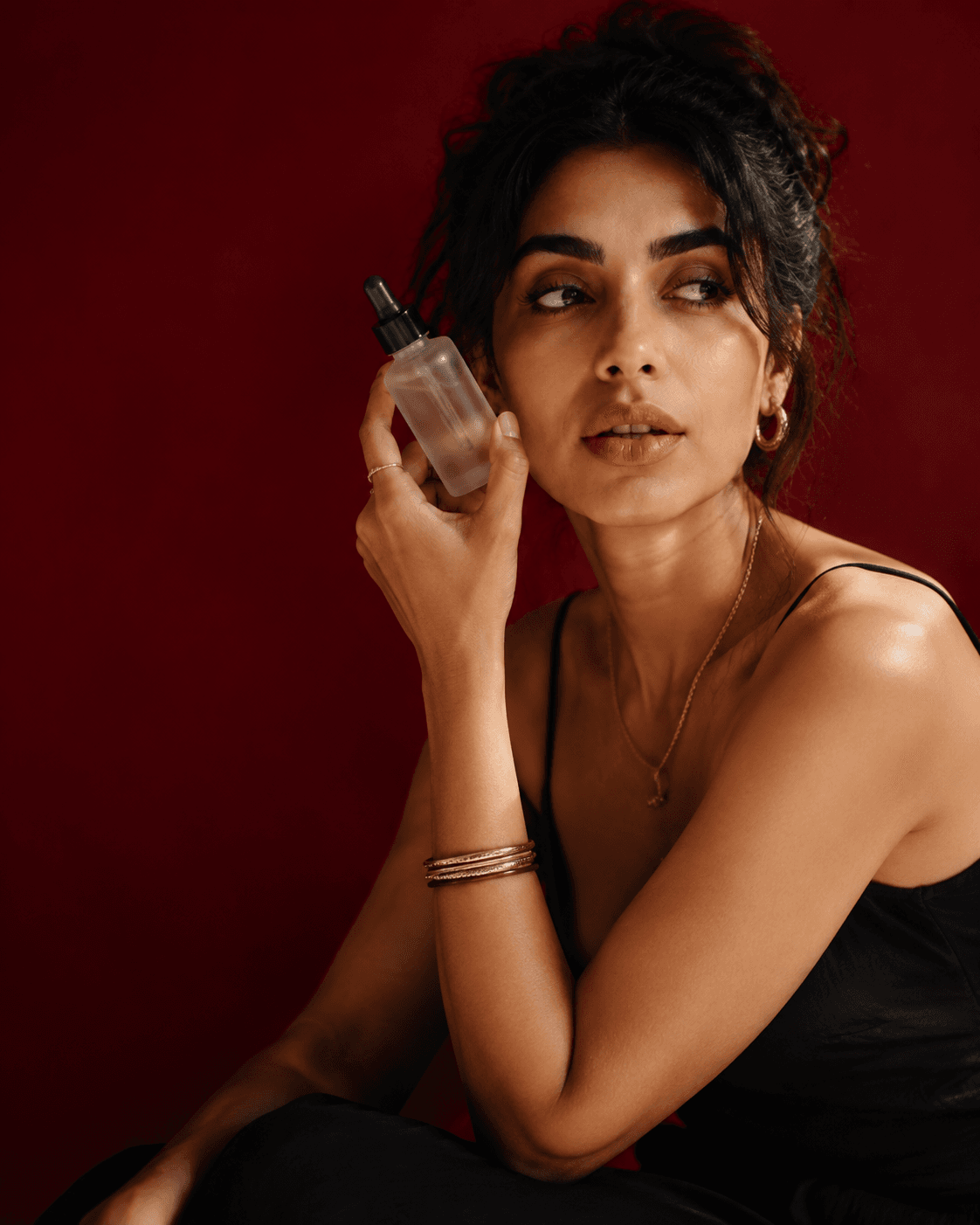 Temporary studio beauty portrait: a woman holding a serum bottle against a deep red background