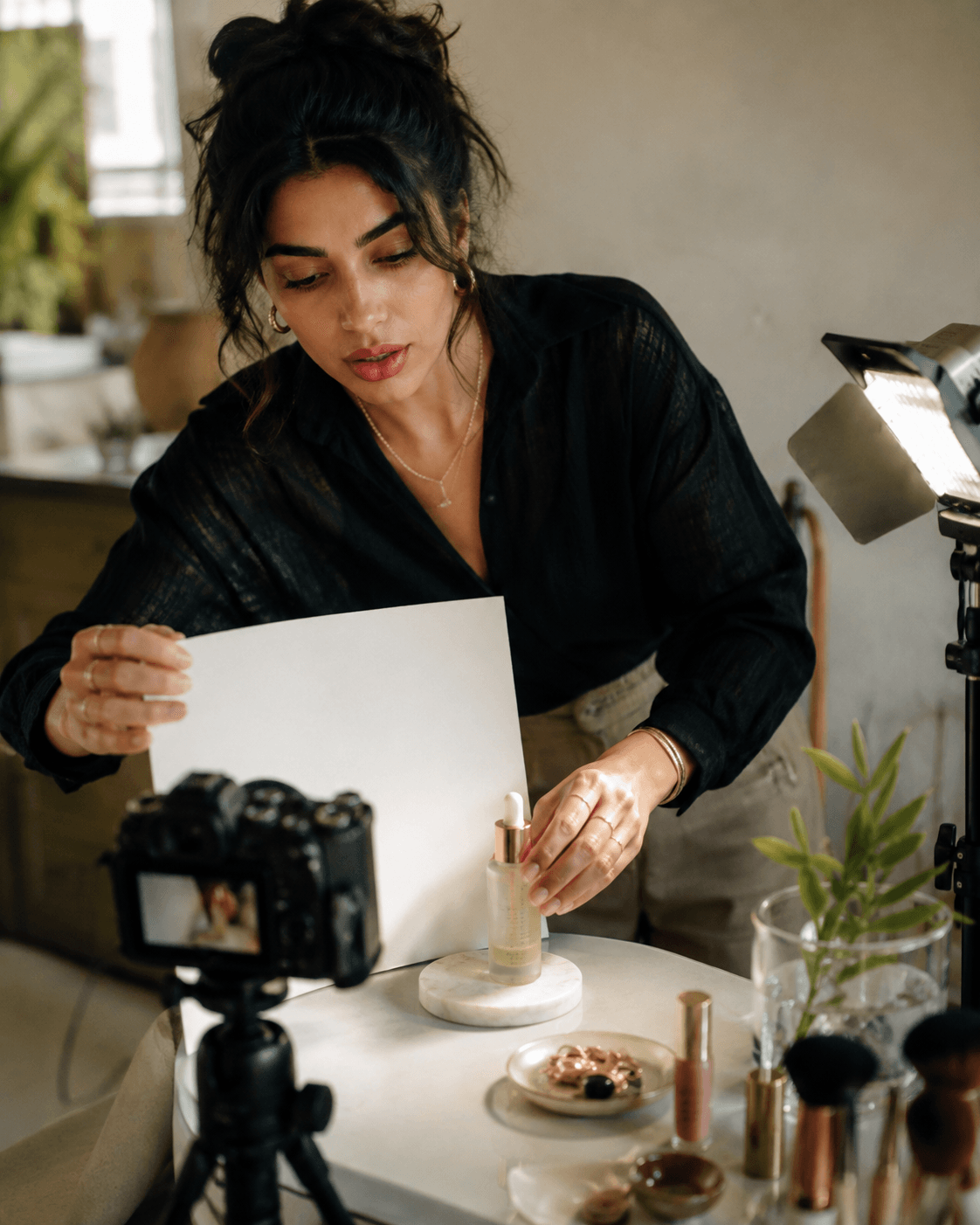 Temporary behind-the-scenes production image: a woman filming herself at a desk with a camera and light