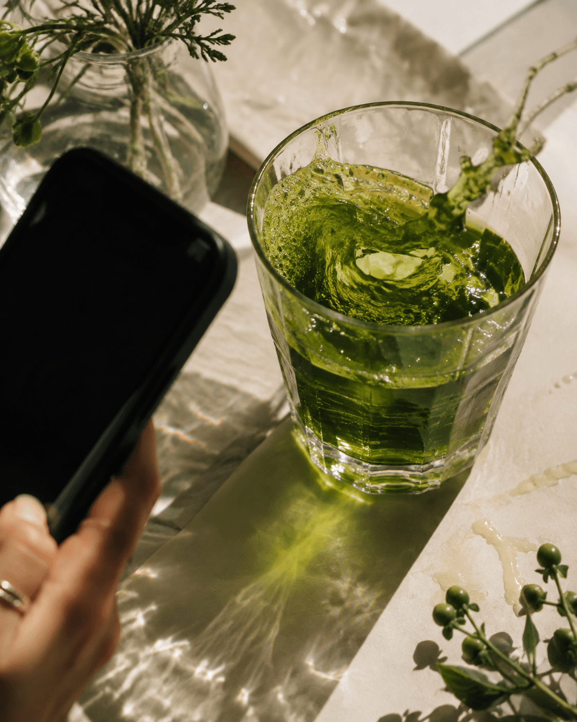 Temporary overhead flat-lay: a phone photographing a green wellness drink in direct sunlight